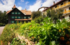 Seminarhotel NaturSinne, © Seminarhotel NaturSinne Ein traditionelles Gebäude mit grünem Fensterladen und einem Garten im Vordergrund unter blauem Himmel.