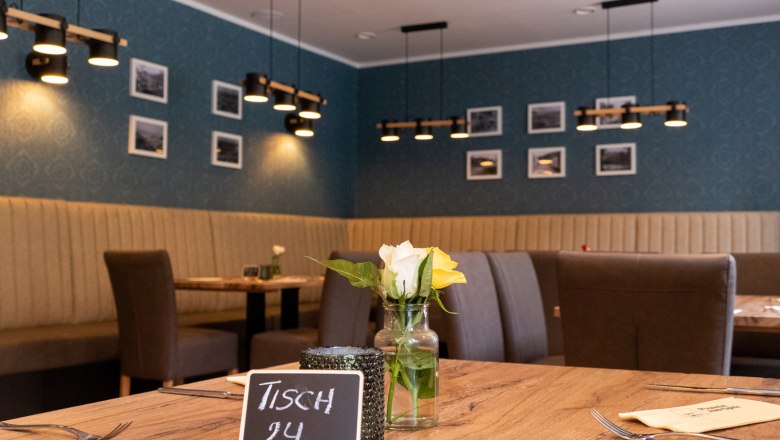 Restaurant-Pizzeria, © Sara Grill Innenansicht eines Restaurants mit Holztisch, Blumen und moderner Beleuchtung.