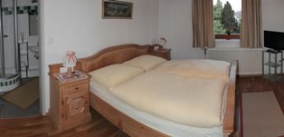 Gästezimmer, © Mühlendorfer Michael Gemütliches Gästezimmer mit Doppelbett, Nachttisch und Fenster mit Vorhängen.