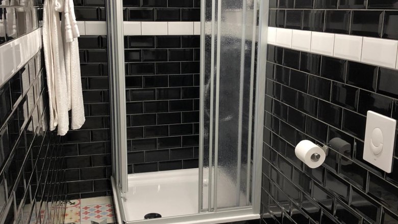 Badezimmer, © Pension zum Spitz Modernes Badezimmer mit schwarzer Fliesenwand, bunter Bodenfliese, Dusche, Handtuch und Toilette.