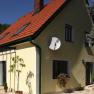 Das Romantik Cottage, © Frau Hahn Gelbes Haus mit rotem Dach und Satellitenschüssel, umgeben von Bäumen.