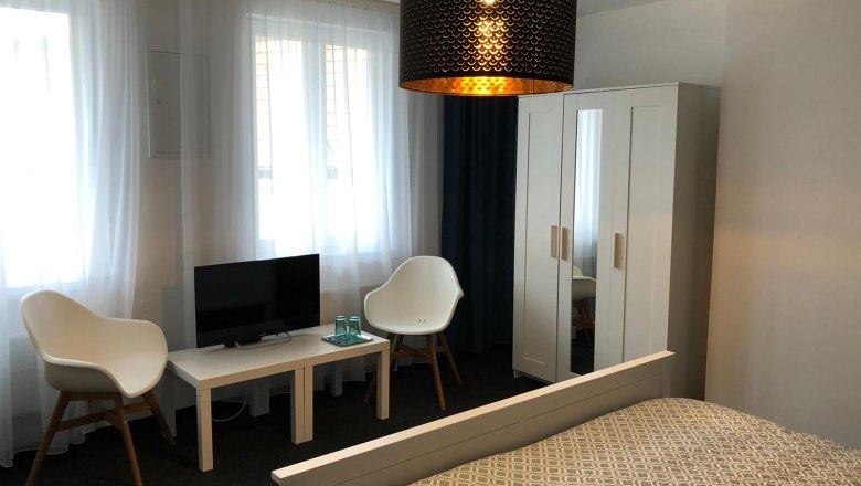 Doppelzimmer, © Pension zum Spitz Modern eingerichtetes Doppelzimmer mit Bett, Schrank, zwei Stühlen, kleinem Tisch und Fernseher.