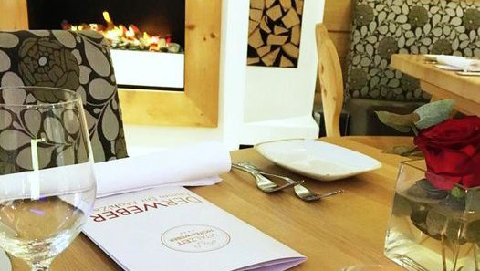 Restaurant DER WEBER, © Familie Weber Innenansicht eines Restaurants mit Tischgedeck, Weinglas, Menü und Kamin.