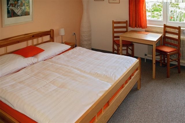Pension Hendling, © Hendling Gemütliches Gästezimmer mit Doppelbett, Holzmöbeln und einem kleinen Tisch am Fenster.