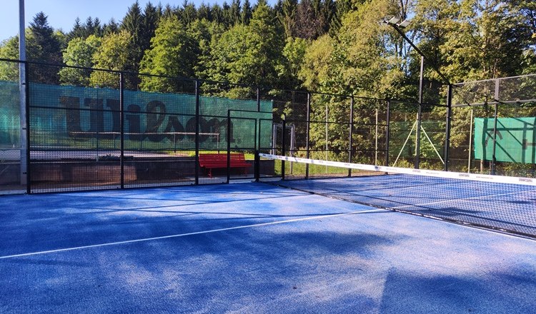 Padeltennis Bad Schönau, © Wiener Alpen Padelplatz mit blauem Boden und Netz, umgeben von Bäumen.