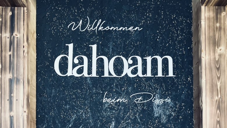 Willkommen im "dahoam", © Anita Gradwohl, dahoam Wand mit Schriftzug 'Willkommen dahoam beim Dissi' und Dekoration.
