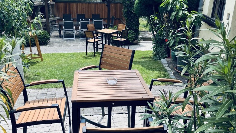 begrünter Gastgarten, © Anita Gradwohl, dahoam Ein gemütlicher Gastgarten mit Holztischen und -stühlen, umgeben von üppigem Grün und Pflanzen.