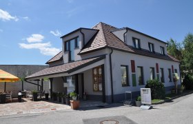 Kölbsls 3, © Thermengemeinden Ein modernes Gebäude mit Terrasse und Sonnenschirm an einem sonnigen Tag.