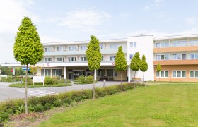 Außenansicht, © Lebens.Med Zentrum Bad Erlach Außenansicht eines modernen Gebäudes mit Bäumen und Rasenfläche.