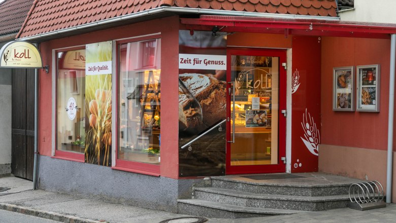 Fachgeschäft mit Café in Wiesmath, © Koll GmbH Eingang der Bäckerei mit Café in Wiesmath, mit roten Wänden und Schildern.