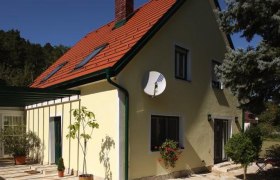 Das Romantik Cottage, © Frau Hahn Gelbes Haus mit rotem Dach und Satellitenschüssel, umgeben von Bäumen.