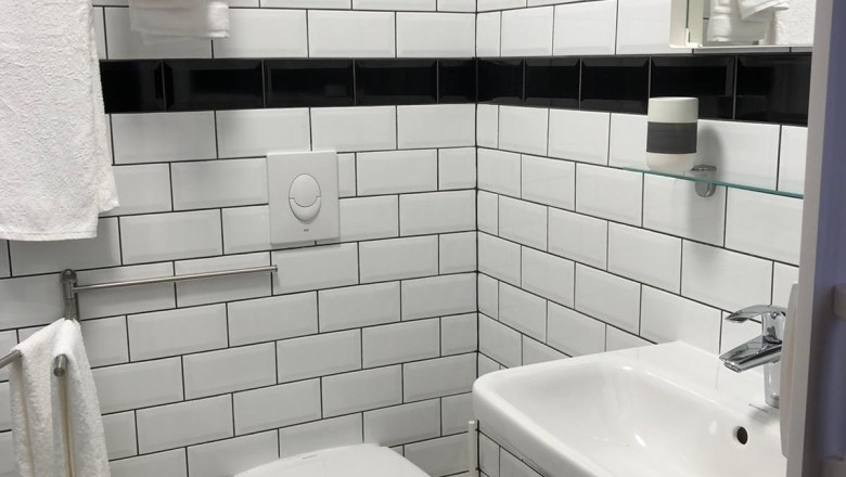 Badezimmer, © Pension zum Spitz Modernes Badezimmer mit weißen Fliesen, Waschbecken und Toilette.