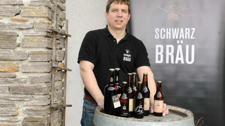Schwarzbräu, © Gerald Schwarz Ein Mann steht hinter einem Holzfass mit Bierflaschen der Marke Schwarzbräu.