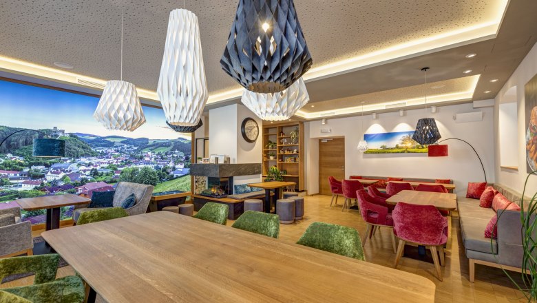 Koll Bistro Kirchschlag, © Koll GmbH Innenansicht eines modernen Bistros mit Holztischen, bunten Stühlen und großen, dekorativen Lampen.