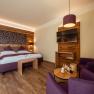 Bett in der Wies‘n, © Niederösterreich Werbung / Maximilian Pawlikowsky Gemütliches Hotelzimmer mit Holzwänden, Doppelbett, TV und lila Sesseln.