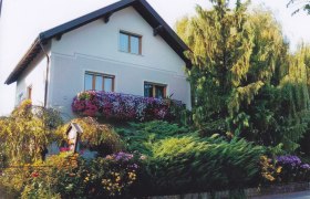 Privatzimmer Familie Kremsl, © Familie Kremsl Ein zweistöckiges Haus mit Blumen auf dem Balkon und umgeben von Bäumen und Sträuchern.