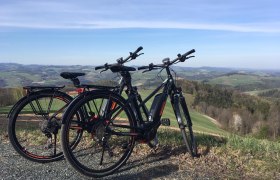 E-Bike-Verleih im Hotel Weber, © Hotel Weber, Michael Giefing Zwei E-Bikes stehen auf einem Hügel mit Blick auf eine hügelige Landschaft.