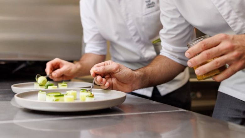 Stefan & Martin Görg, © Philip Styrer Zwei Köche in weißen Kochjacken richten Gourmetgerichte auf weißen Tellern an.