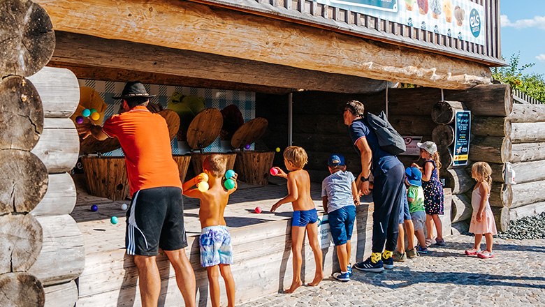 Eis-Greissler Erlebnispark Eiskugel werfen, © Blochberger Eisproduktion GmbH Kinder und Erwachsene werfen bunte Bälle in einem Spielstand aus Holz im Freien.