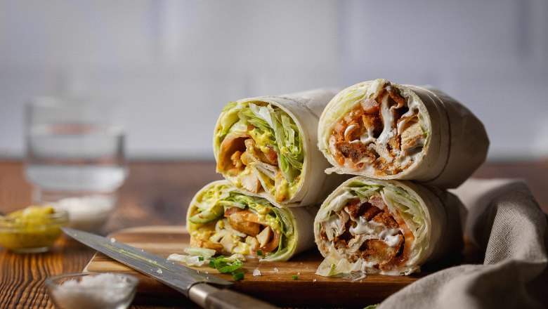 Wraps, © Koll GmbH Vier aufgeschnittene Wraps mit Salat und Fleischfüllung auf einem Holzbrett.