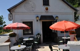 Nest aussen, © Thermengemeinden Außenansicht eines Cafés mit Terrasse, Tischen und Sonnenschirmen.