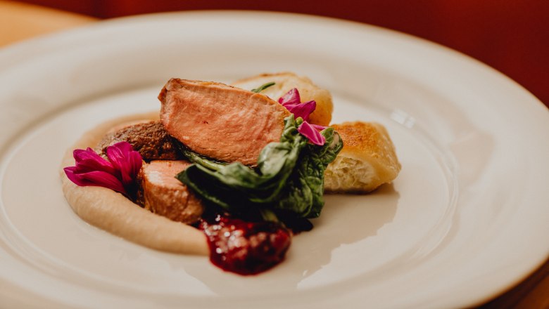 Rosa gebratene Ente mit Rahmtascherl & Maroni-Püree, © Niederösterreich Werbung/Klaus Engelmayer Ein Teller mit rosa gebratener Ente, Rahmtascherl, Maroni-Püree und grünen Blättern, garniert mit essbaren Blüten.