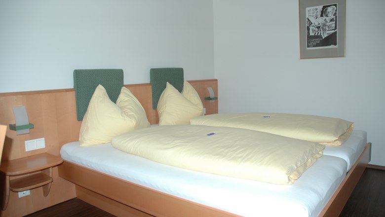 Hotel Zur Alten Schule, © Viregro Capital Gmbh Hotelzimmer mit Doppelbett, gelber Bettwäsche und Wandbild.