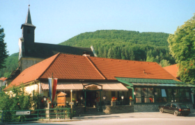 Landgasthof Thaler, © Thaler Ein Landgasthof mit rotem Dach vor einem bewaldeten Hügel.