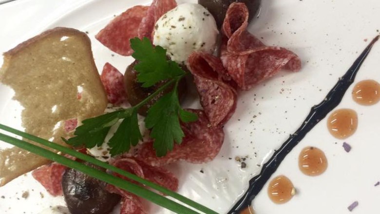 Köstliches aus der Küche, © Gasthof Martin Windbichler Ein Teller mit Salami, einem Ziegenkäsebällchen, Kräutern und einem Stück Brot.