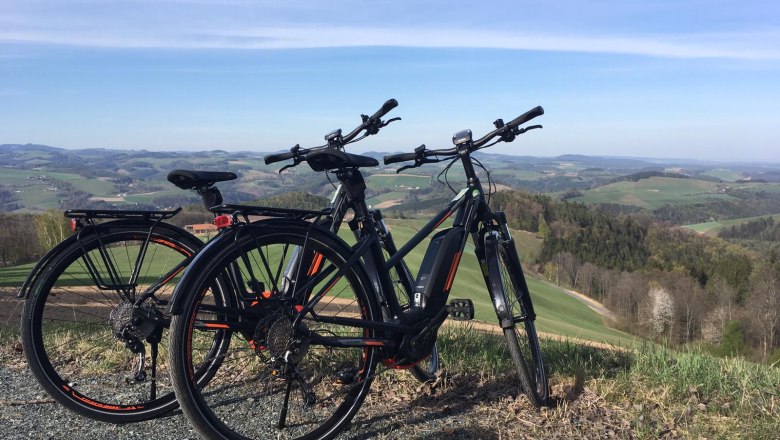 E-Bike-Verleih im Hotel Weber, © Hotel Weber, Michael Giefing Zwei E-Bikes stehen auf einem Hügel mit Blick auf eine hügelige Landschaft.