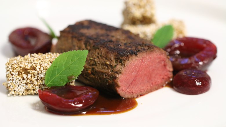 Köstliches aus der Haubenküche, © Familie Görg Gourmetgericht mit rosa gebratenem Fleisch, Obst und Kräutern auf einem weißen Teller angerichtet.