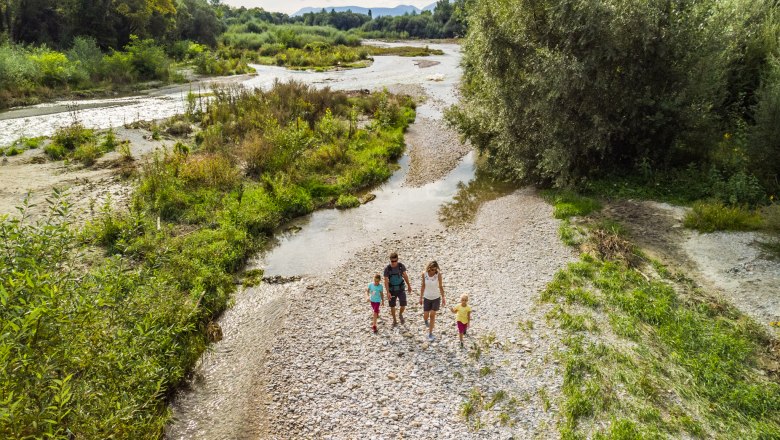 In der Leitha-Au, © Wiener Alpen, Martin Fülöp Eine Familie spaziert durch eine grüne Flusslandschaft mit Kieselsteinen und Bäumen. Luftaufnahme