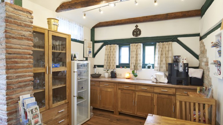 Frühstücksraum, Gästezimmer Victoria, © Marianne Graf Ein gemütlicher Frühstücksraum mit Holzmöbeln, einem Kühlschrank, einer Kaffeemaschine und dekorativen Holzbalken an der Decke.