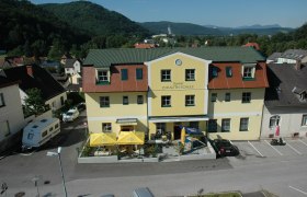 Hotel Zur Alten Schule, © Viregro Capital Gmbh Gelbes Gebäude mit der Aufschrift 'Gasthof Zur Alten Schule', umgeben von Hügeln und Bäumen.