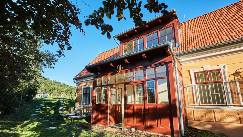 Villa Tranquillini, © Herbert Lehmann Eine gelbe Villa mit roten Dachziegeln und einem verglasten Eingang, umgeben von Bäumen und einem grünen Garten.