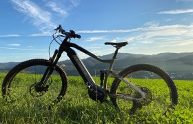 Radverleih direkt im Hotel, © Manuel Stockinger Nahaufnahme eines Fahrrads auf grüner Wiese mit Hügellandschaft im Hintergrund.