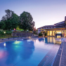 Beleuchtete Poolanlage bei Nacht mit Gebäuden im Hintergrund.
