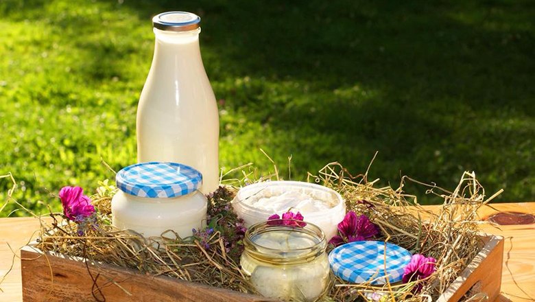 Eine Flasche Milch und Gläser mit Milchprodukten auf Heu in einer Holzkiste, dekoriert mit Blumen.
