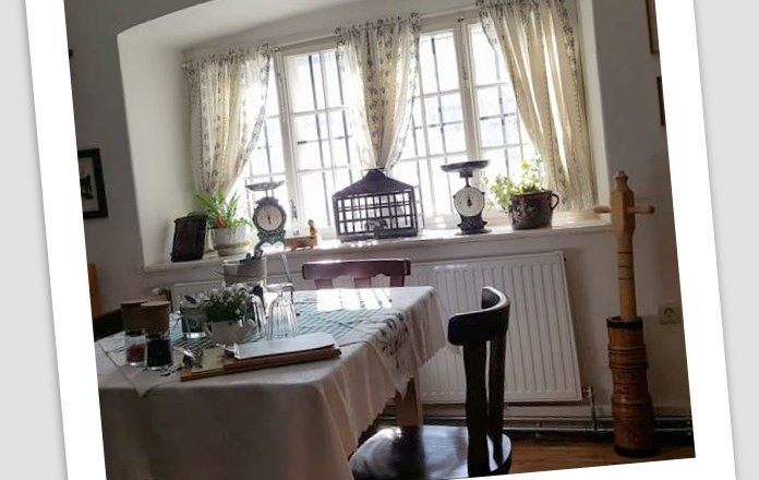 Gem&uuml;tlicher Essbereich mit Tisch, St&uuml;hlen und Fenster mit Vorh&auml;ngen.