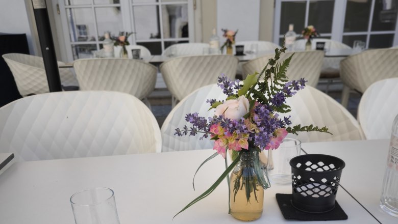 Gedeckter Tisch auf einer Terrasse mit Blumenstrauß und Besteck.