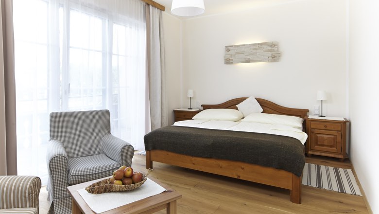 Helles Zimmer mit Doppelbett, Sessel und Tisch mit Obstschale.