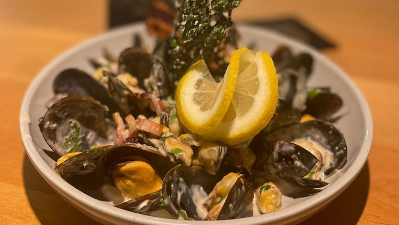 Ein Teller mit Muscheln, Sahnesoße und Zitronenscheiben auf einem Holztisch.