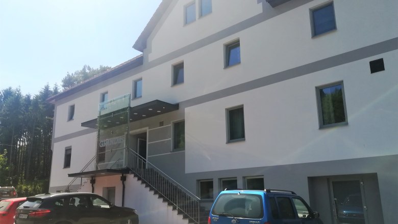 Au&szlig;enansicht eines modernen Gasthauses mit mehreren Fenstern und parkenden Autos davor.