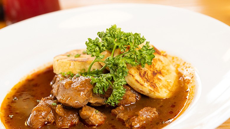 Ein Teller mit Rindsgulsch und Knödeln mit Petersilie garniert.