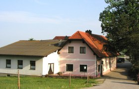 Ein traditionelles Gasthaus mit rosa und weißen Wänden und einem roten Ziegeldach, umgeben von grüner Landschaft.