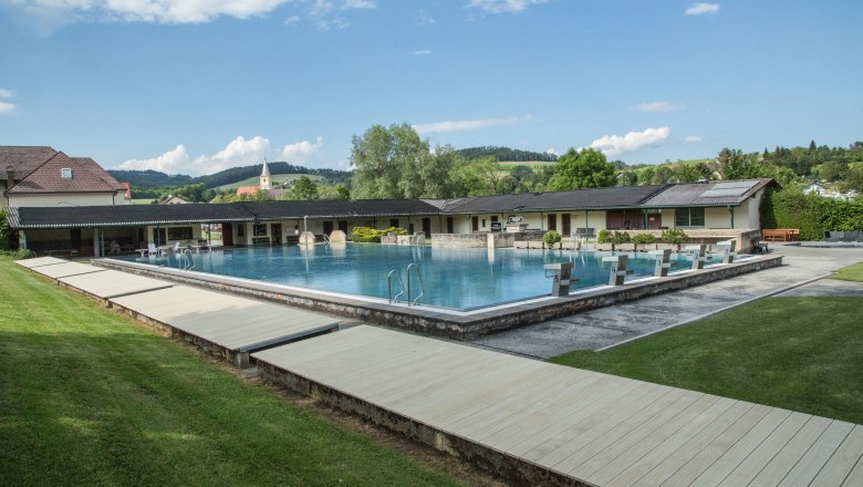Freibad Krumbach mit Schwimmbecken und Sprungbl&ouml;cken, umgeben von gr&uuml;ner Landschaft und Geb&auml;uden.