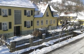 Gelbes Haus im Winter mit Schnee bedeckt, umgeben von einem Zaun und Bäumen.