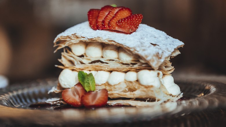 Eine Cremeschnitte mit Blätterteig, Sahne und Erdbeeren auf einem Teller.