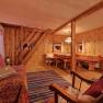 Gemütliches Wohnzimmer mit Holzwänden, Sofa, Schaukelstuhl und Esstisch. Rustikales Ambiente mit Teppich und warmem Licht.
