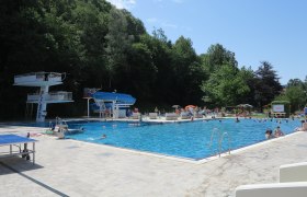 Ein Freibad mit Sprungturm, Rutsche und vielen Badeg&auml;sten an einem sonnigen Tag.